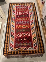 Top-down photo of a rectangular tribal rug showing the full rug with multicolored geometric designs and fringed edges.