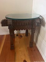 Front angle of wooden tribal side table with glass top showing carved details on legs and sides.