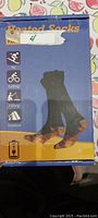 Blue box packaging showing black and grey heated socks with icons indicating suitability for skiing, cycling, fishing, and outdoor use.