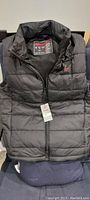 Black Flybare heated vest laid flat showing front side with zipper and hang tag attached.