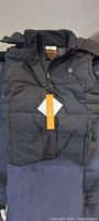 Front view of black puffer heated vest with hood and zipper, showing the Caforu heat control logo on the chest area.