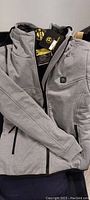 Grey heated jacket folded with visible front zipper and a small logo patch on the chest.