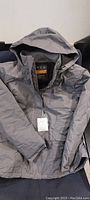 Full front view of grey jacket with hood, zipped closed, lying flat.