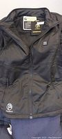 Photo of front of black Ptahdus heated vest showing zipper, collar, and branding.
