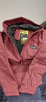 Full view of red hooded heated jacket showing front zipper and hood, interior black lining visible.