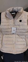 Front view of large tan padded heated vest with a zippered front and logo patch on the chest.