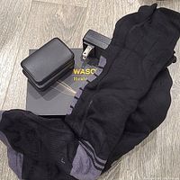 Photo showing one pair of black heated socks with grey accents, a charger with plug, and the box labeled 'Wasoto Heated Socks'.