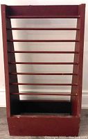 Front view of a rectangular burgundy wooden magazine rack with horizontal slats and solid base