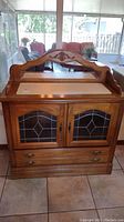 Full front view of oak buffet showing glass paneled double doors with decorative leaded glass and lower drawer.