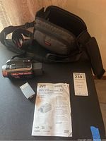 JVC camcorder with carrying case, battery charger adapter, and manual on a dark surface.