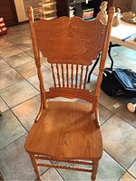 Front view of a single dining chair showing wood carving details on backrest and turned spindle supports.