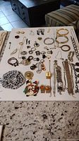 Full overview of costume jewelry including bracelets, rings, pins, earrings, cufflinks laid flat on white surface