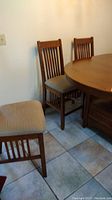Photo showing three wooden dining chairs around a round wooden table with upholstered seats in beige patterned fabric.