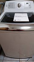 Front view of white Kenmore Elite top-load washer with user manual on lid