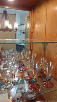 Photo showing all six glasses inside a wooden cabinet with mirrored background, highlighting the amethyst and blue designs on the stems and bases of four wine glasses and the two musical notation goblets.