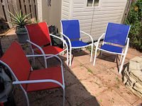 All four outdoor chairs arranged showing two with red canvas and two with blue canvas seats, white aluminum frames visible