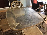 Top view showing textured glass tabletop with umbrella hole and bronze/gold-tone aluminum frame edges.