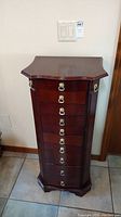 Front view of tall narrow wood jewelry cabinet with 9 drawers and brass ring pulls