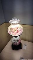 Full view of electric converted oil lamp showing floral glass shade with ruffled top and floral decorated glass body on ornate metal base.