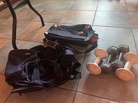 Photo showing black luggage bag, black Atlantic bag, and four hand weights (two silver, two white) on floor.