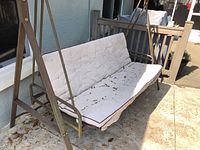 Outdoor three seat swing glider with white removable cushions showing dirt stains.