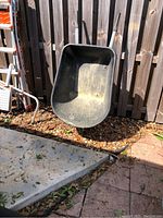 Full view of the black plastic wheelbarrow tub showing wear and dirt inside