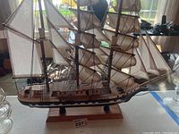 Full view of the wooden model ship on a wooden base with fabric sails and rigging.