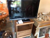 Sony Bravia 40 inch LCD TV on top of the wooden TV cart with remote and manual placed on the cart shelf.