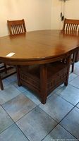 Wide angle of rectangular wooden pub table with two chairs, showing the top surface and base shelf and storage drawer.
