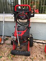 Front view of the Troy-Bilt pressure washer showing the pressure gauge, hose wrapped around the frame, and wand attached.