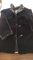 Front view of black deep pile plush fabric coat showing the toggle buttons and fur collar trim.