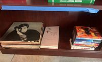 Shelf with stacked vinyl records and DVD cases, showing the collection's variety and quantity.