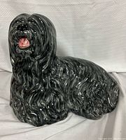 Front side view of a glazed ceramic dog statue with an open mouth showing pink tongue and teeth, with black and gray marbled fur texture, glossy finish.