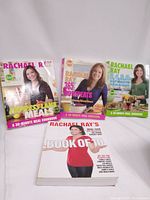 Four Rachel Ray cookbooks placed vertically showing front covers with titles prominently displayed.