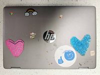 Top view of HP Chromebook x360 laptop showing silver case with multiple colorful stickers including hearts and other images.