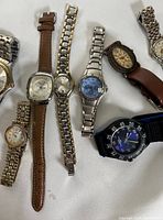 Nine mixed wristwatches arranged flat showing their dials and strap styles including leather, metal link, and fabric strap.