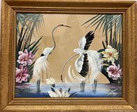 Photo of framed watercolor painting featuring two white cranes and floral elements with a background of palm fronds and water.