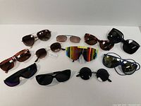 Full collection photo showing 11 different sunglasses with various frame and lens styles laid out on white background.