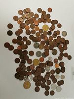 Overview of a large assortment of US and Canadian coins spread on a flat surface showing a mix of pennies, nickels, quarters and other denominations, various conditions including some copper, silver and gold color coins.