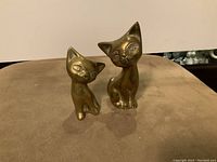 Front view of two brass cat sculptures showing carved details and polished finish.