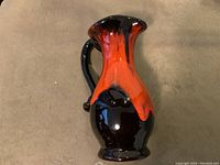 View of the front of the Canuck ceramic pitcher showing red lava glaze dripping over black base, emphasizing glaze texture and pitcher shape.