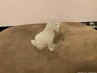 Front angle view of a white onyx Highland Terrier figurine showing the shape, detailing on ears and face, sitting on a brown surface.