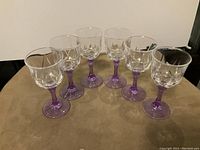 Set of 6 Cristal D Arques-Durand Auteuil Lilas wine glasses arranged on a brown surface, showing clear bowls with embossed floral patterns and purple stems.