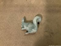 Side view of small light gray ceramic squirrel figurine by George Wade, showing the squirrel holding a nut and its curled tail.