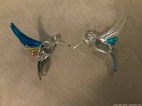 Two glass hummingbird figurines positioned facing each other showing side and front views.