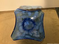 Top view of the cobalt blue glass bowl showing white drip glaze pattern inside and square handkerchief shape.