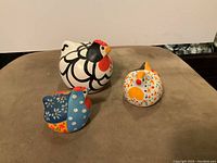 Top view of the three hand painted hen figurines showing vibrant colors and designs on a beige surface.