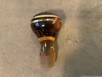 Amber glass decanter stopper with gold trim on rounded top and frosted fitting base shown from above angle.