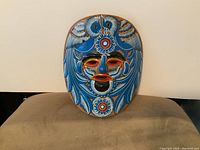 Front view of handmade ceramic Mexican folk art mask with detailed blue, white and red painted design and facial features.
