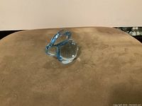 Blue crystal glass bunny figurine viewed from one side on a brown surface.